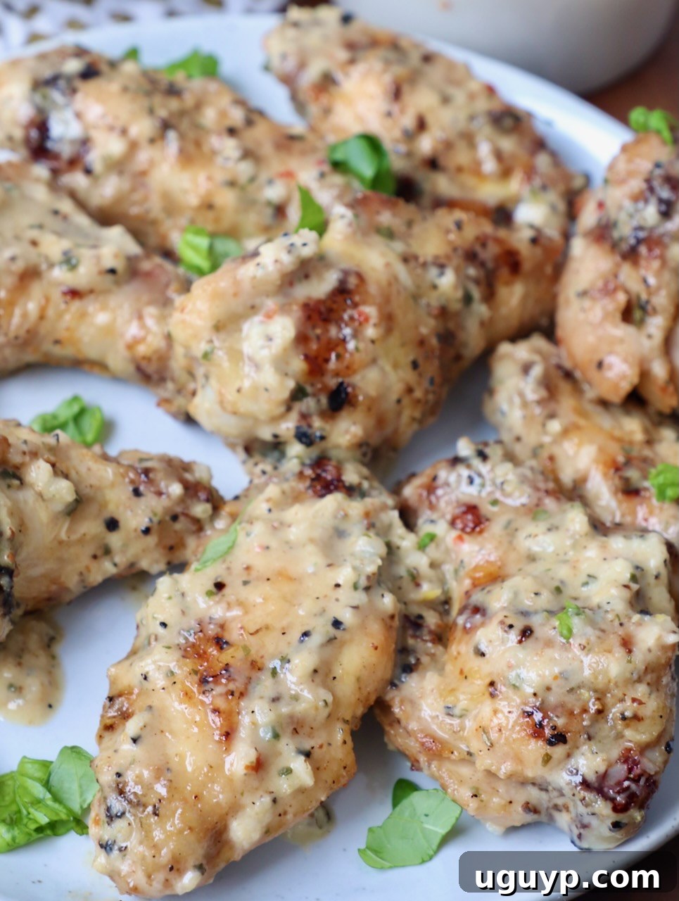 Garlic Parmesan grilled chicken wings garnished with fresh herbs on a white plate, showcasing the delicious sauce.