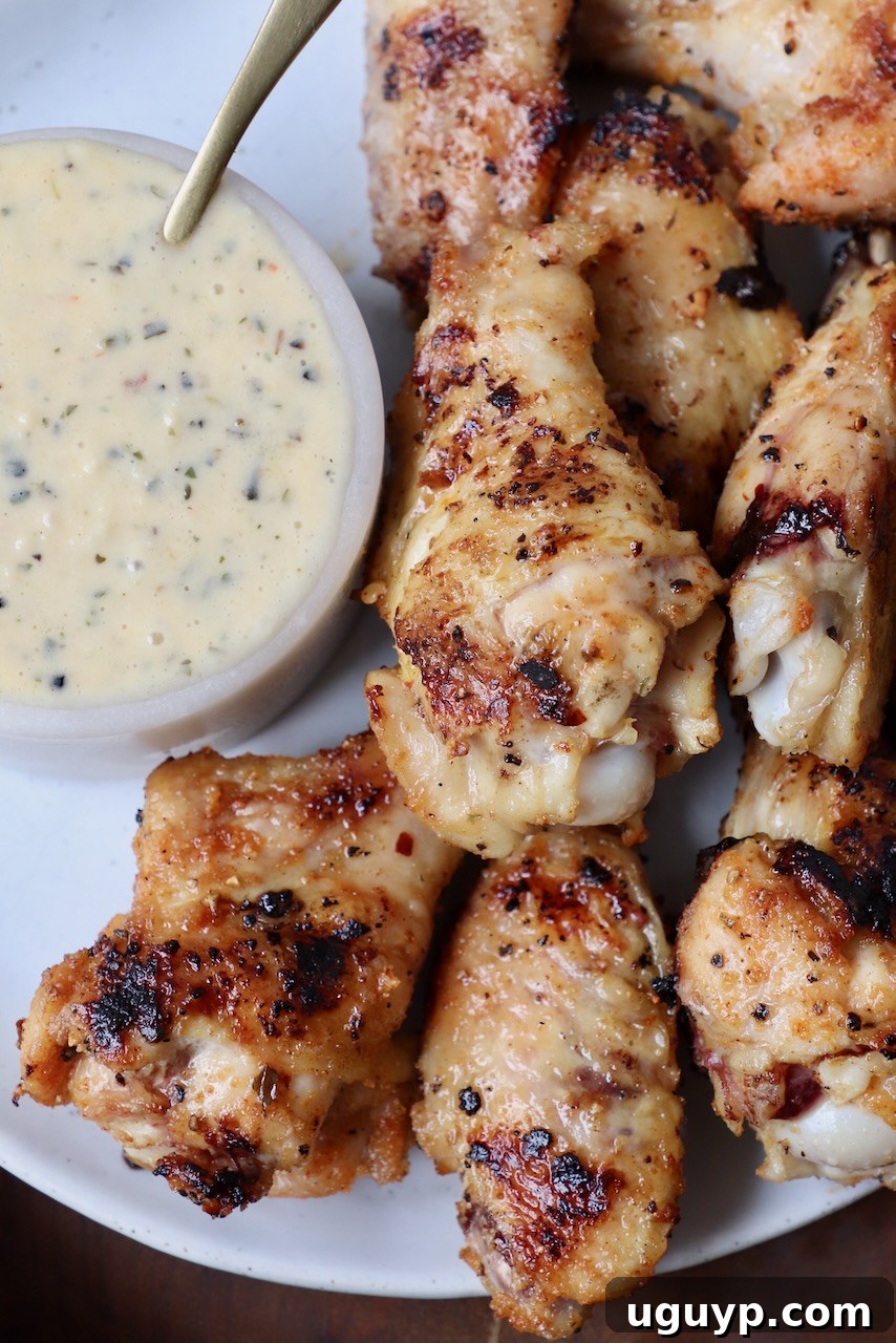 Perfectly grilled chicken wings arranged on a plate with a small bowl of creamy garlic parmesan sauce on the side, ready to be enjoyed.