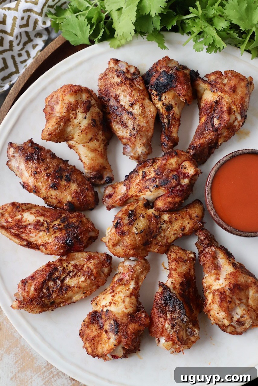 A plate of grilled chicken wings, some sauced and some plain, with a small bowl of buffalo sauce on the side for dipping.