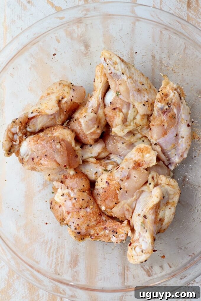 A close-up shot of seasoned chicken wings glistening with olive oil and spices in a glass bowl.