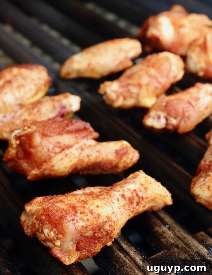 Raw seasoned chicken wings carefully placed in an even layer on hot grill grates, ready to cook.