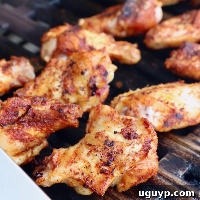 Grilled chicken wings, now with a crispy, golden-brown exterior, continuing to cook on the grill.