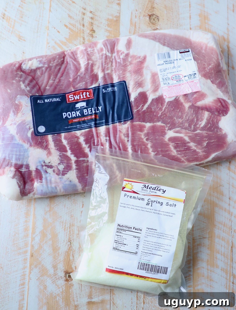 Raw pork belly with curing salt ready for seasoning on a white wooden board.
