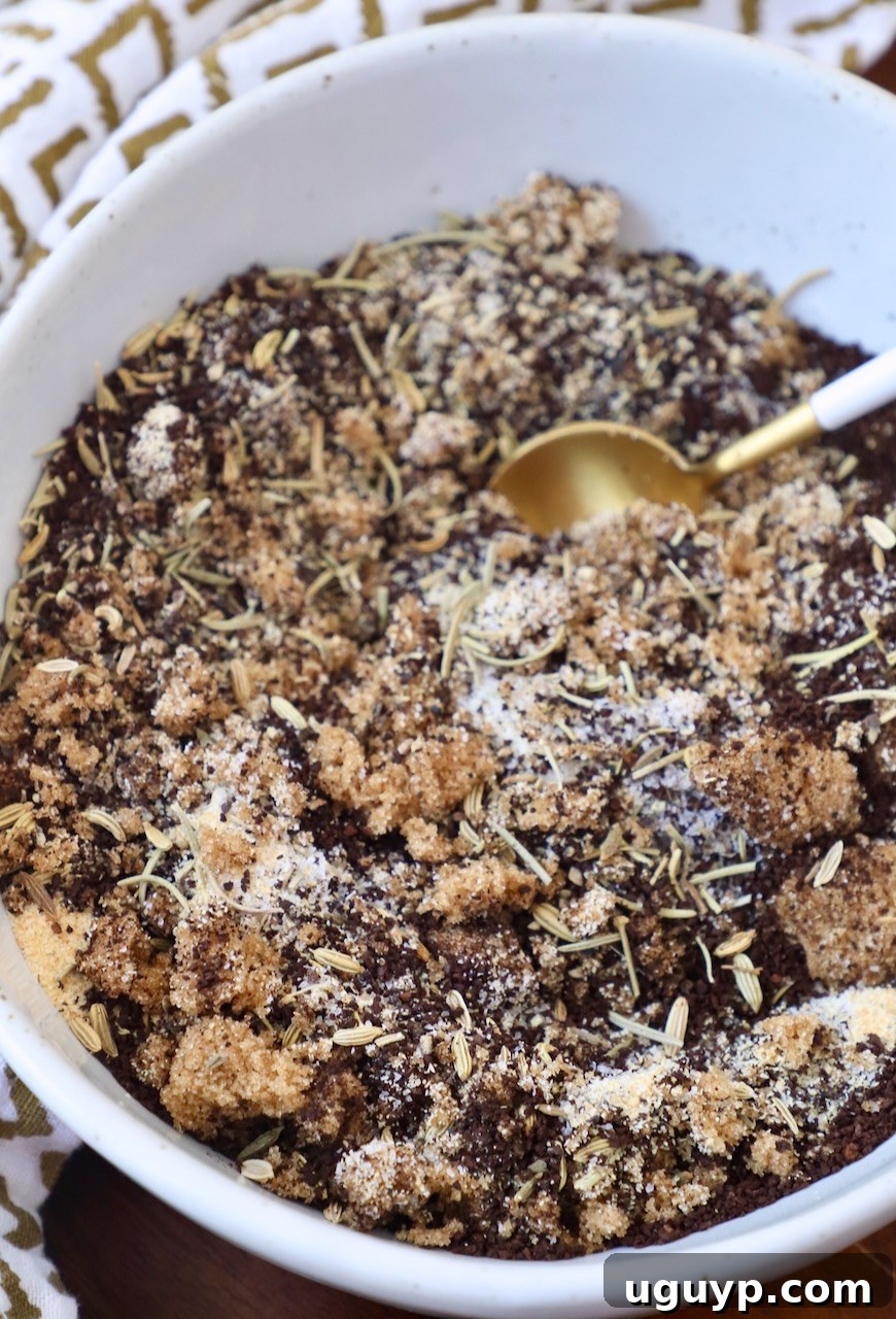 A close-up of ground coffee, brown sugar, and various dried herbs meticulously mixed in a bowl, with a small spoon resting inside, highlighting the rich textures and colors of the Coffee Steak Rub.