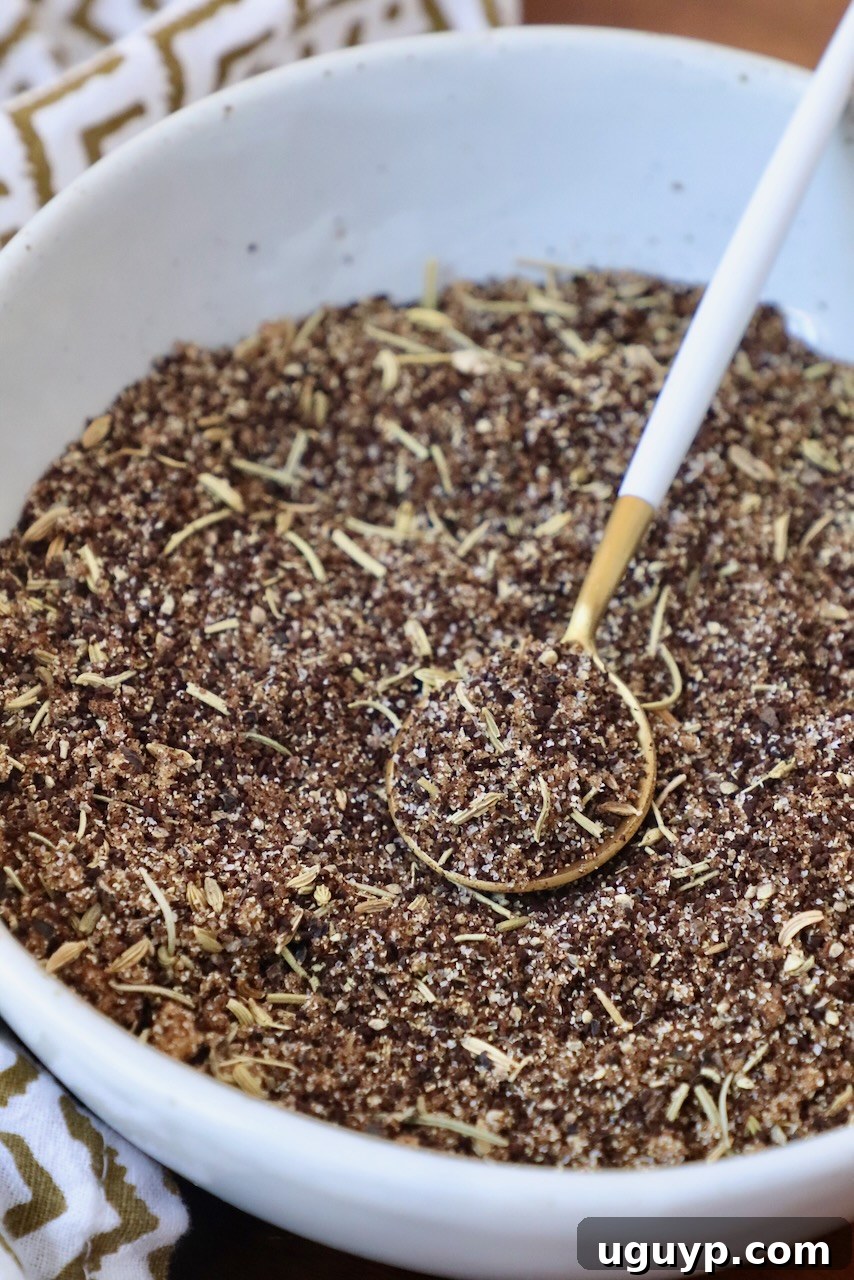 A small glass bowl filled with the freshly mixed coffee steak rub, with a miniature wooden spoon resting in it, showcasing the rich, dark, and textured blend.