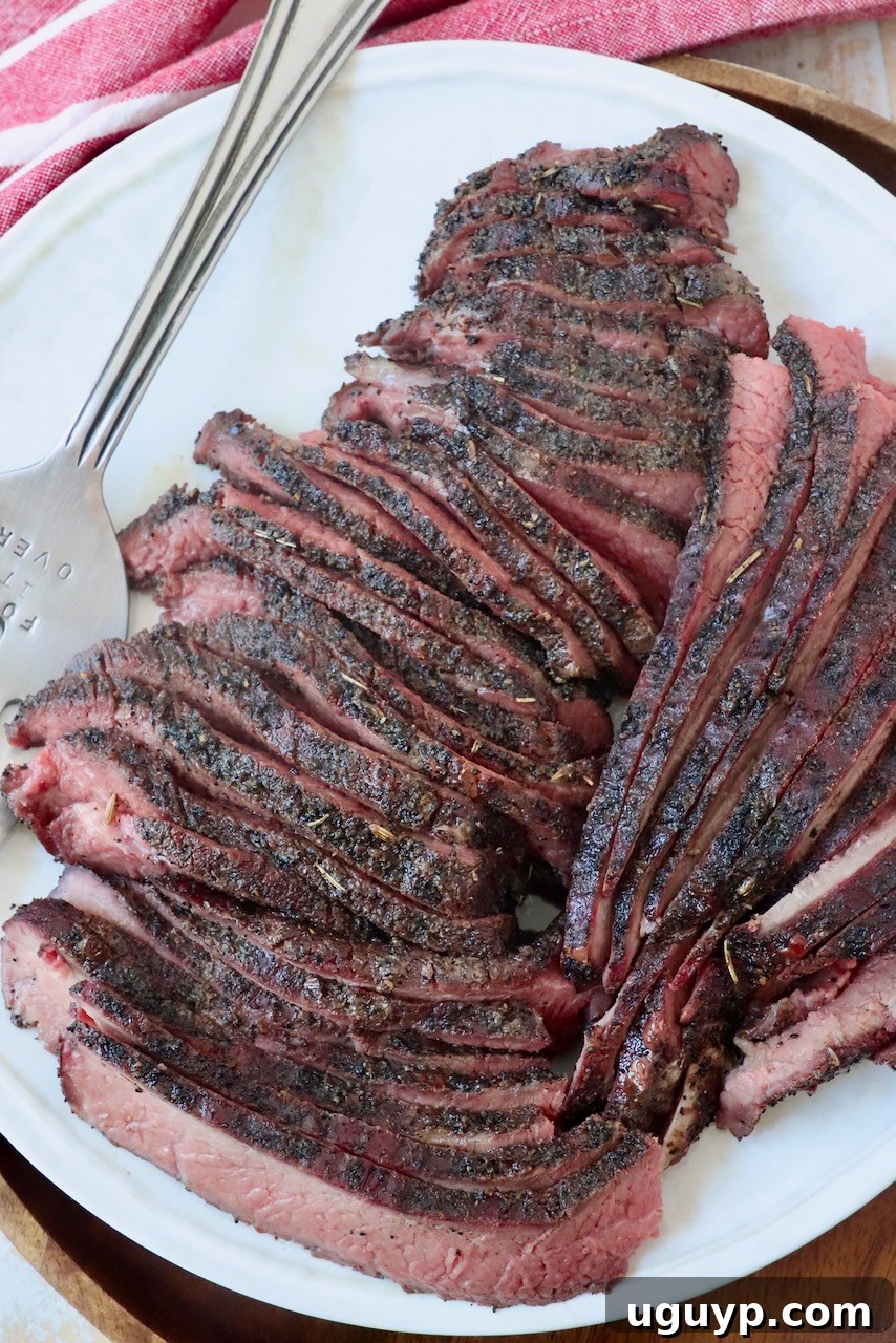 Slices of perfectly cooked, coffee-crusted smoked tri-tip are arranged on a plate, with a serving fork nearby, showcasing the dark, flavorful crust and tender interior.