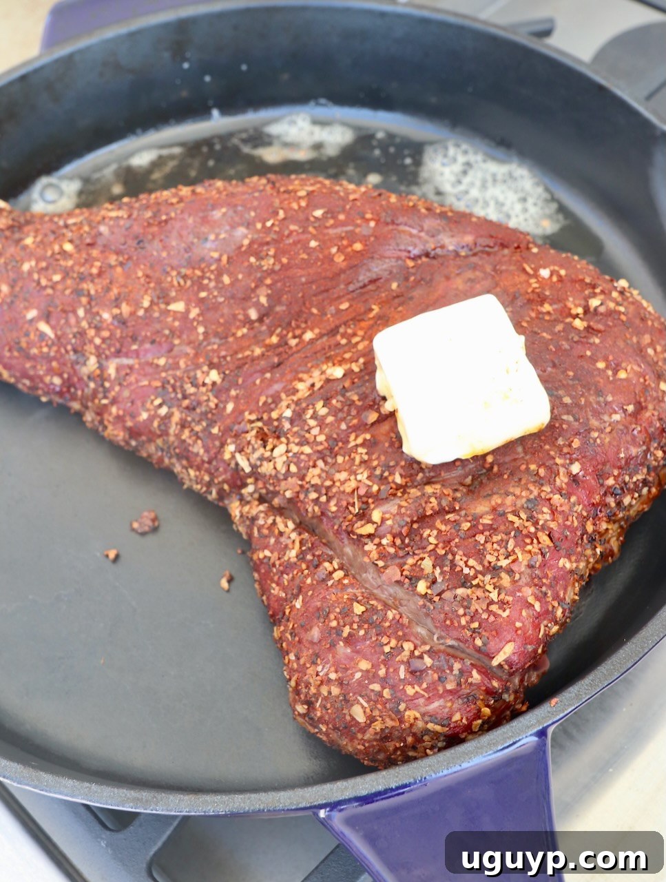 Smoked and seasoned tri tip roast resting in a cast iron skillet, topped with melting butter for searing.
