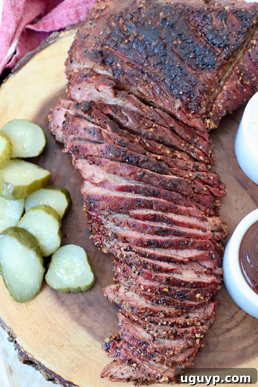 Generously sliced smoked tri tip on a cutting board, accompanied by pickles, showcasing its perfect doneness and crust.