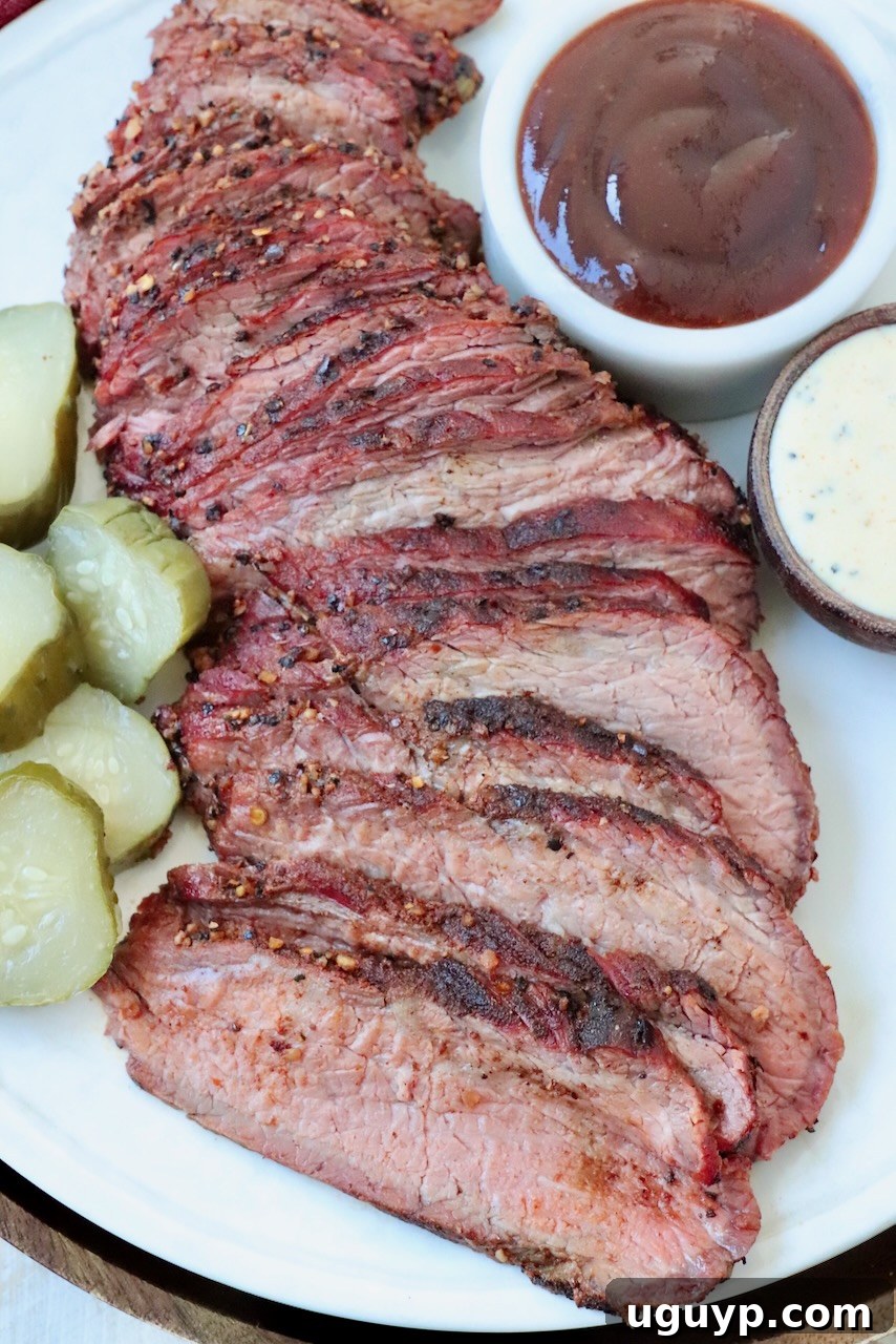 Beautifully sliced smoked tri tip on a plate, garnished with BBQ sauce and sliced pickles, ready to be served.