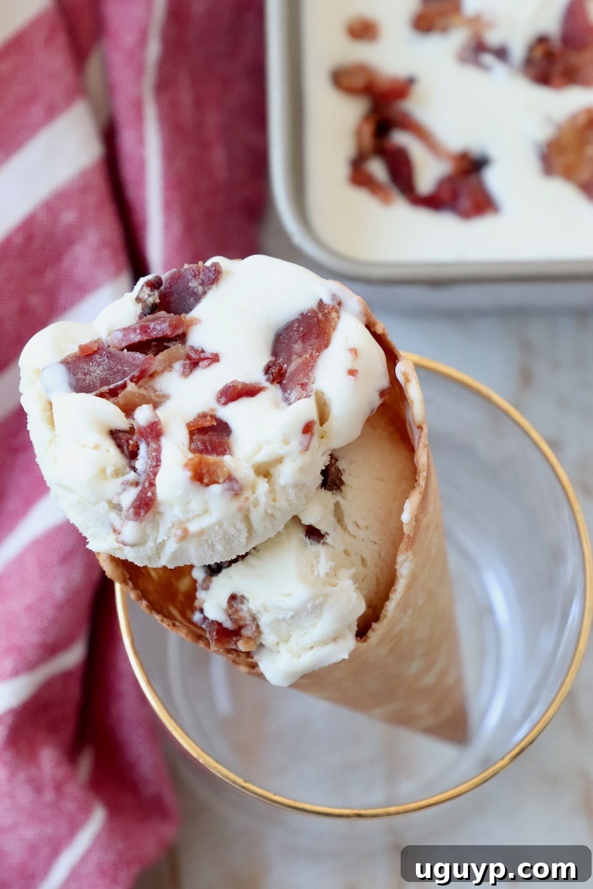 Two scoops of maple bacon ice cream elegantly served in a waffle cone, held in a glass