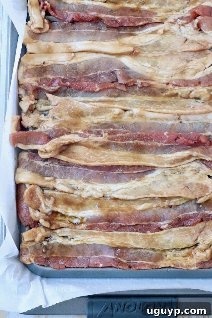 Uncooked strips of thick-sliced bacon arranged on a wire rack over a foil-lined baking sheet