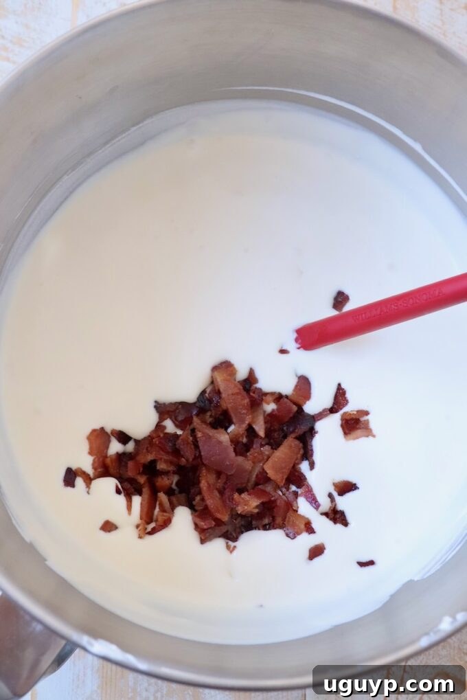 Chopped candied bacon being gently folded into the ice cream base mixture in a bowl