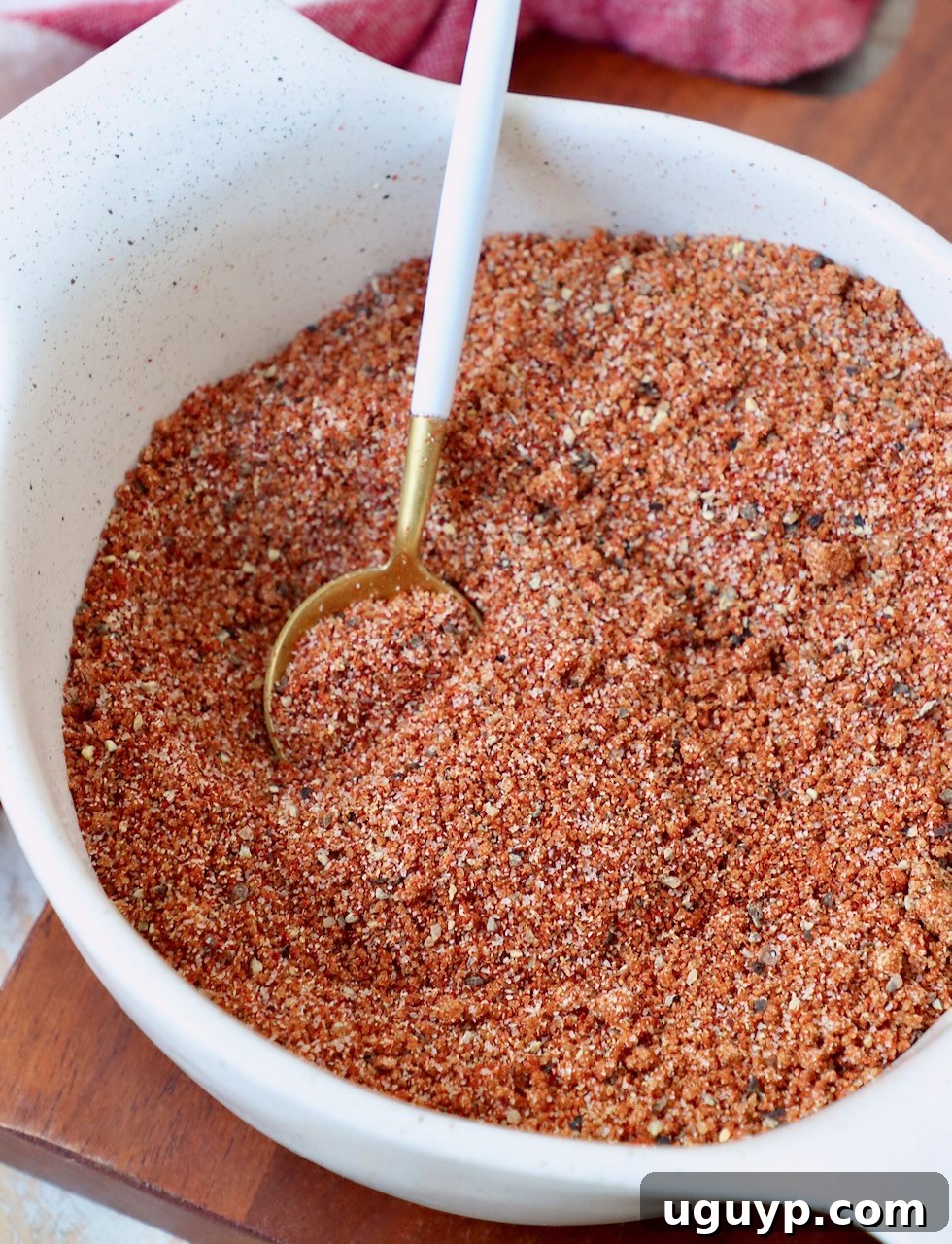 A bowl filled with homemade BBQ seasoning blend, featuring a small wooden spoon dipped into the rich, reddish-brown spice mix, ready for use.