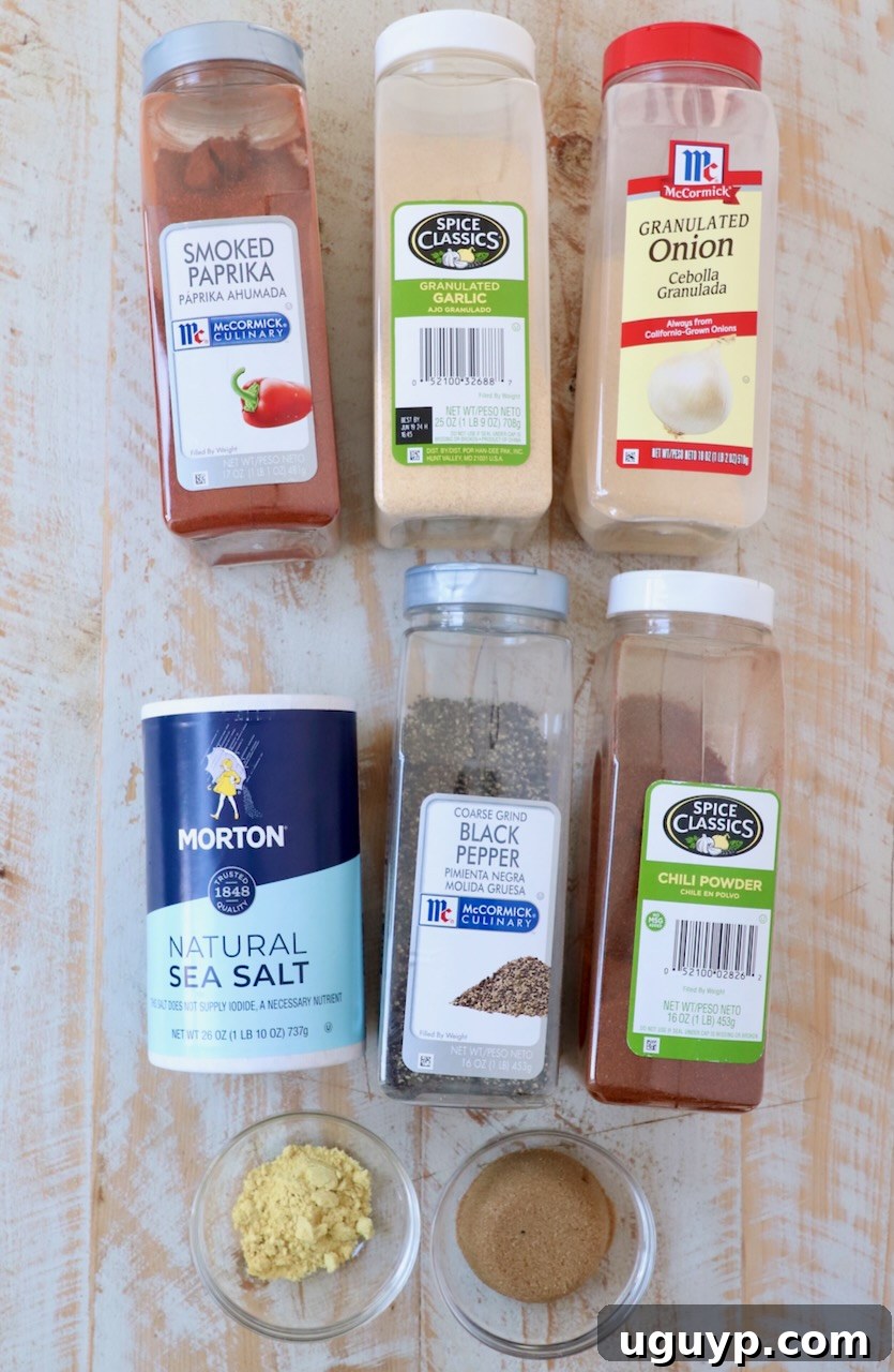 Various spices for homemade BBQ seasoning laid out on a white wooden board, including brown sugar, smoked paprika, garlic powder, onion powder, salt, pepper, chili powder, and mustard powder.