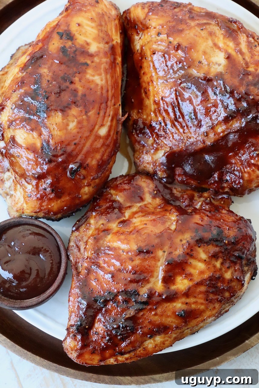 Two grilled chicken breasts, generously covered in a glossy BBQ sauce, resting on a white plate.