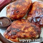 Grilled BBQ chicken breasts on a plate with a side bowl of BBQ sauce, invitingly presented.