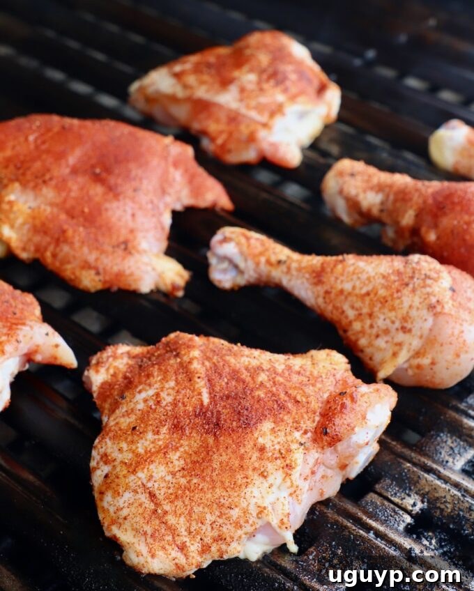 Seasoned chicken pieces carefully arranged on the unlit side of a hot grill, ready for slow cooking.