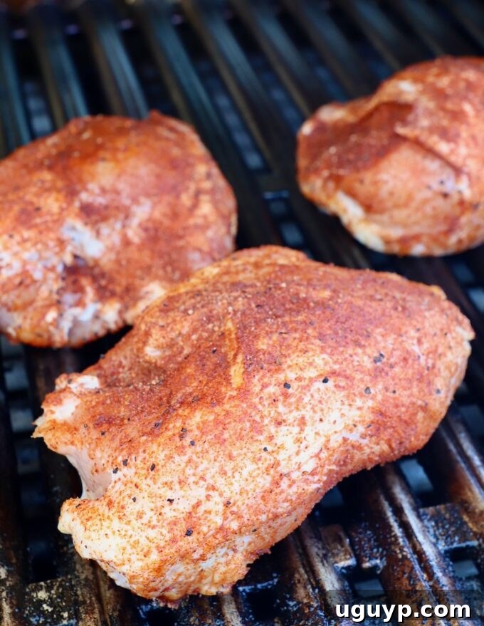 Close-up of seasoned chicken breasts cooking slowly on the indirect heat zone of the grill.
