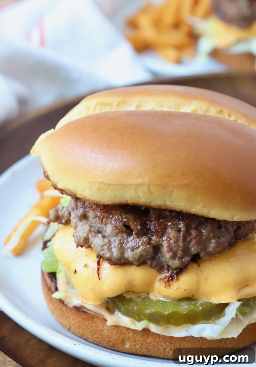 Two cheesy smash burgers stacked on a toasted bun, garnished with fresh lettuce and tomato, served on a plate.
