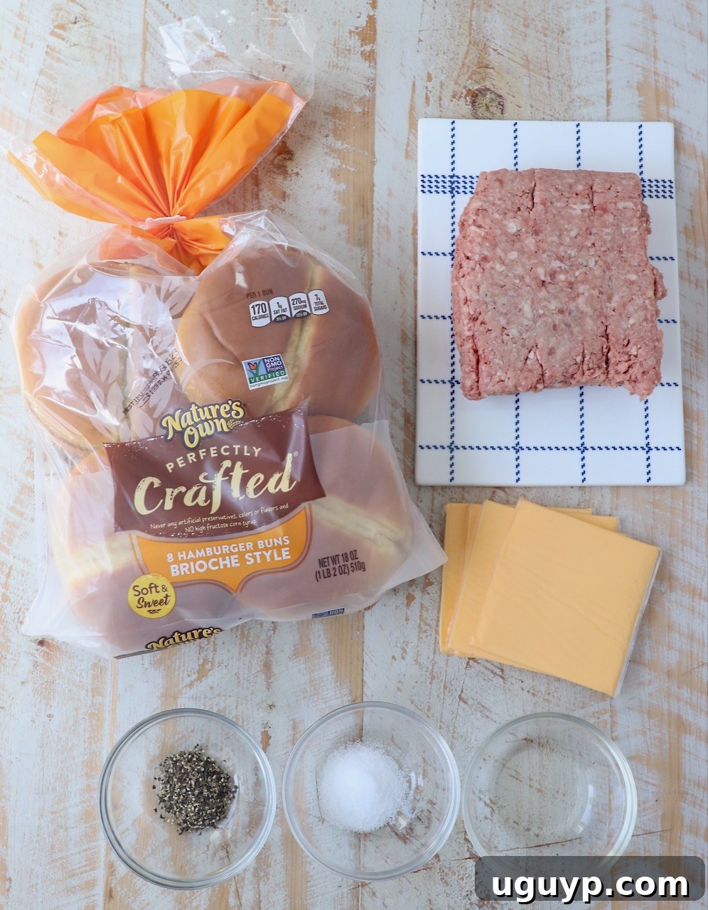 Ingredients for homemade smash burgers laid out on a white wooden board: ground beef, vegetable oil, hamburger buns, cheese slices, salt, and pepper.