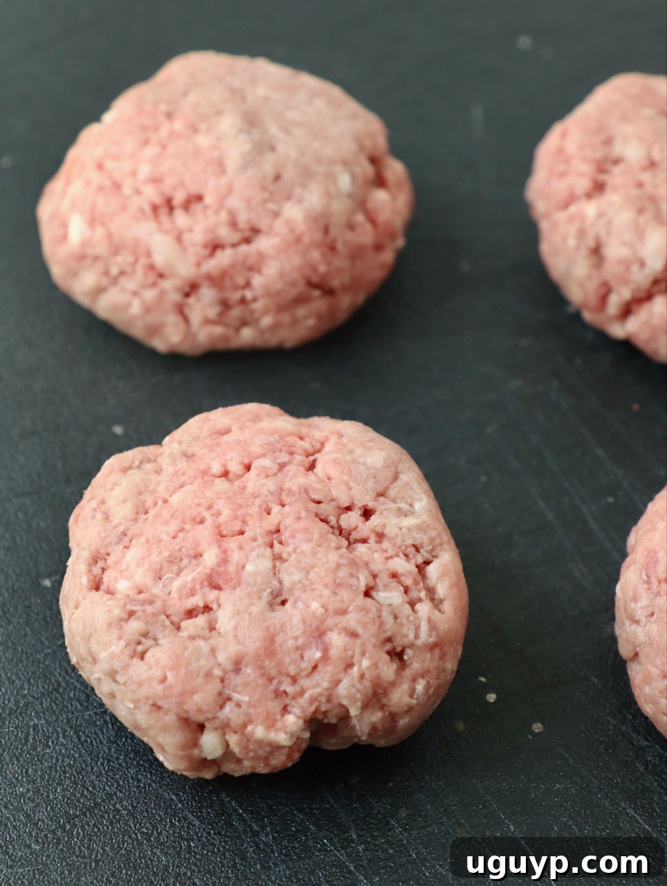 Portioned balls of seasoned ground beef on a cutting board, ready to be smashed.