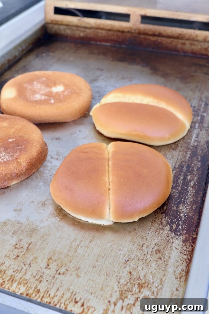 Hamburger buns toasting face-down on a hot griddle, achieving a golden brown crust.