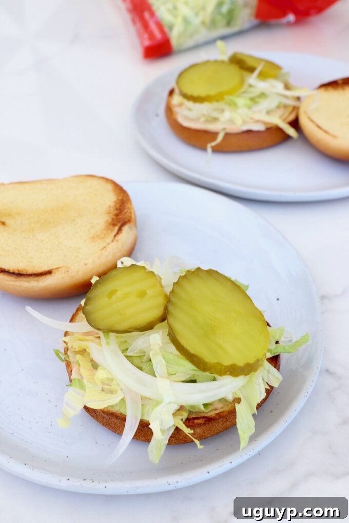 Toasted hamburger bun bottoms, prepped with burger sauce, shredded lettuce, sliced onions, and dill pickles.