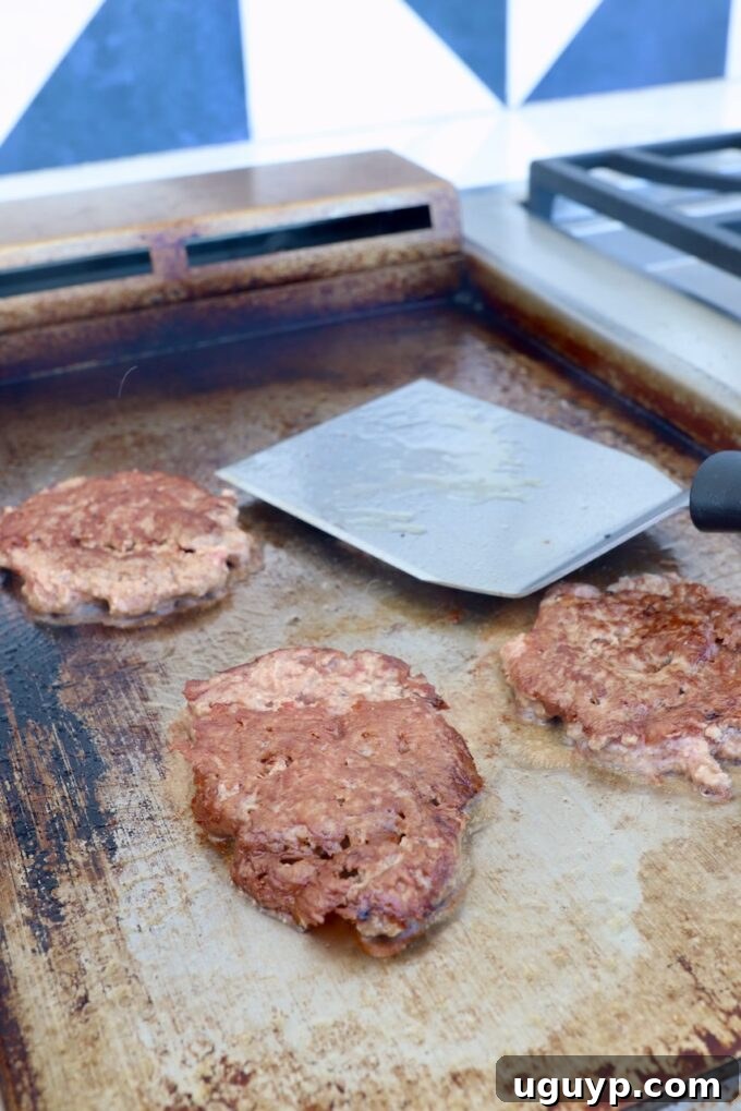 Ground beef balls being smashed into thin patties on a hot griddle, developing a crispy crust.