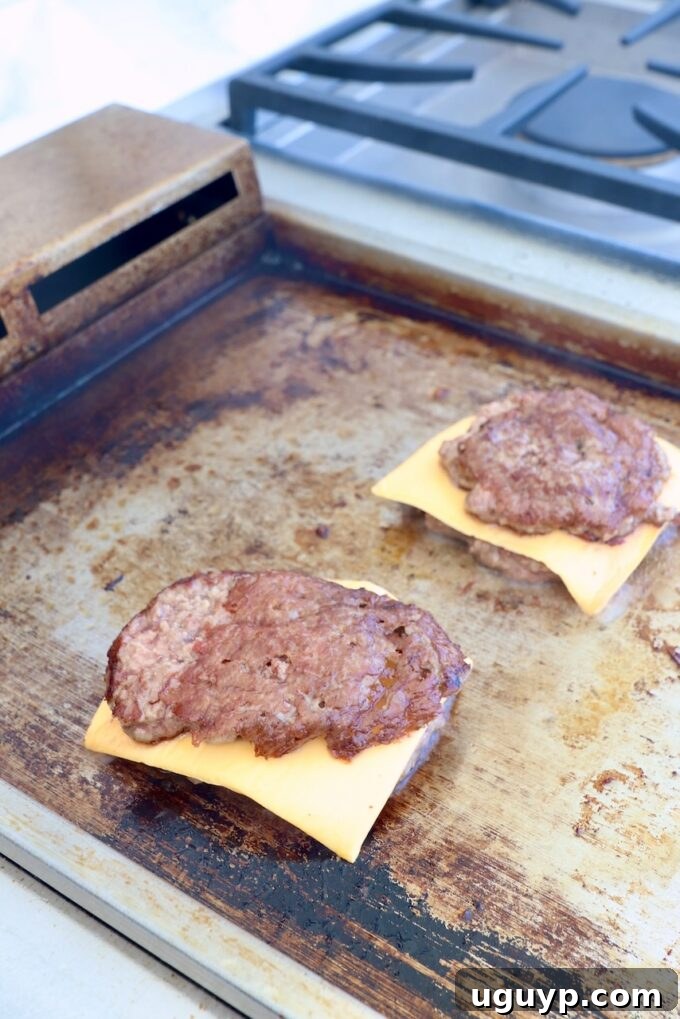Smashed burger patties on the griddle, some topped with melting slices of American cheese.