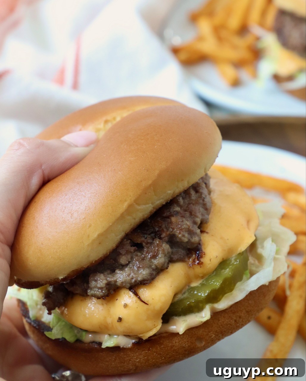 A hand holding a perfectly assembled double smash cheeseburger, showcasing its crispy patties and melted cheese.
