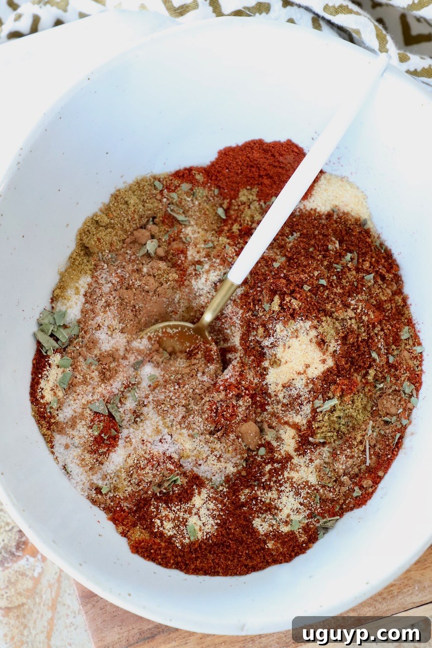 A bowl of vibrant homemade enchilada seasoning with a spoon, surrounded by individual spices like chili powder, cumin, and paprika, ready to be mixed