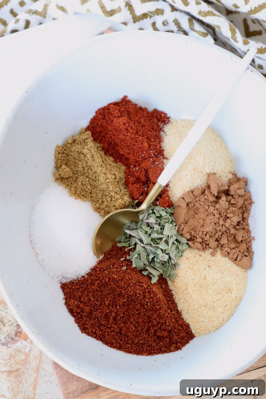 A small bowl filled with a homemade enchilada seasoning blend, with a spoon resting inside, showcasing the rich color and texture of the spices