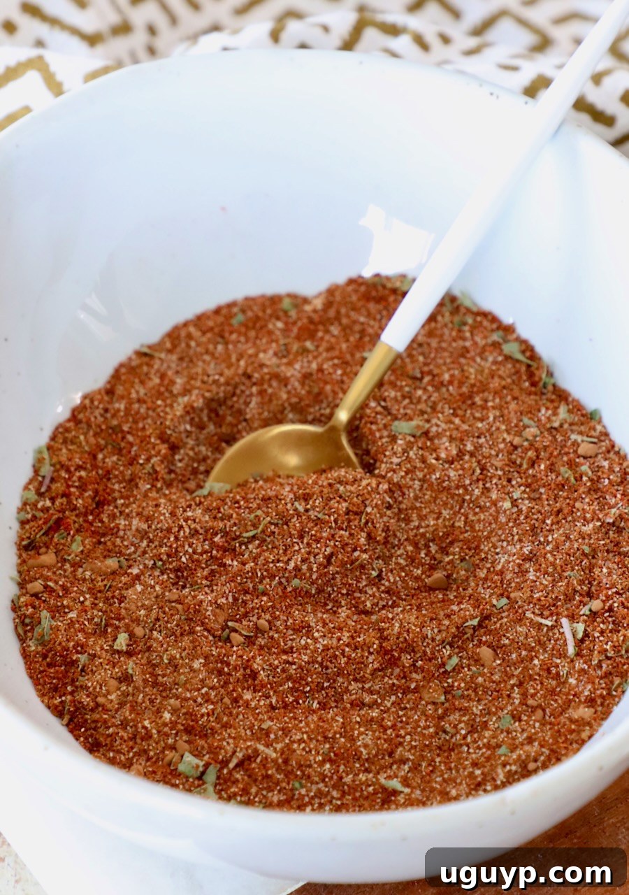 A close-up shot of homemade enchilada seasoning in a small bowl with a measuring spoon, highlighting its rich color and fine texture