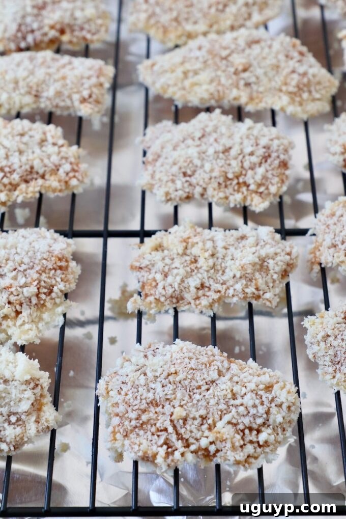 uncooked breaded chicken pieces neatly arranged on a wire rack over a foil-lined baking sheet