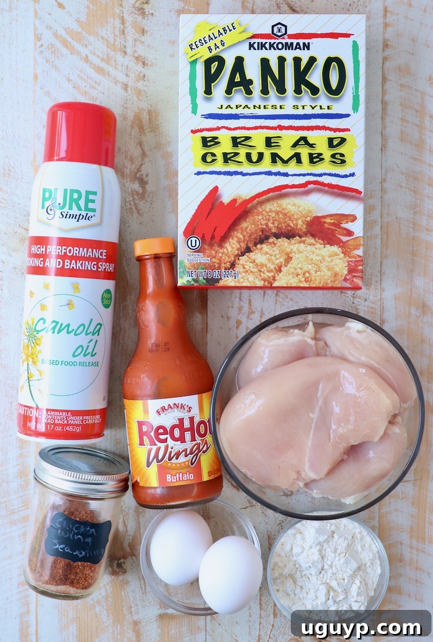 ingredients for boneless wings on white wood board, including chicken breast, eggs, flour, panko, seasoning, and buffalo sauce