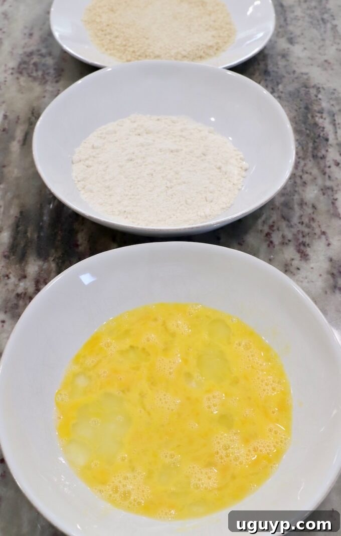 three bowls on countertop: one with whisked egg, one with all-purpose flour, and one with panko breadcrumbs