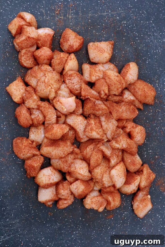 cubes of chicken breasts generously tossed with chicken wing seasoning on a wooden cutting board