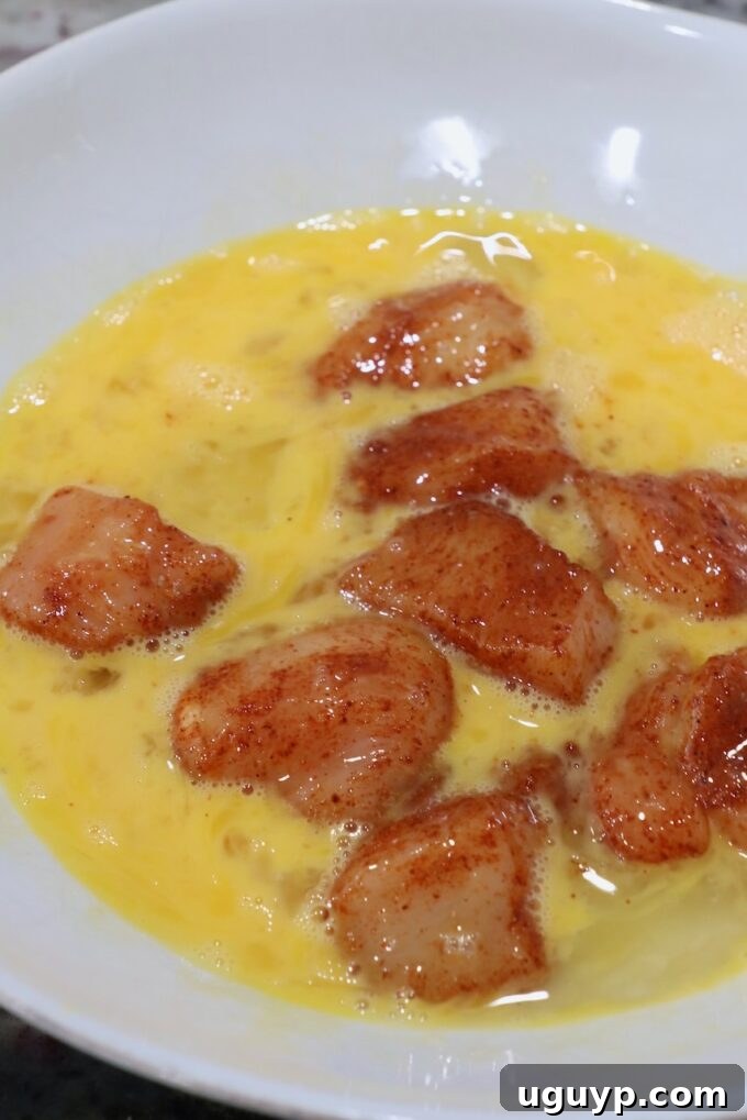 seasoned pieces of chicken breast being dipped into a bowl of whisked eggs