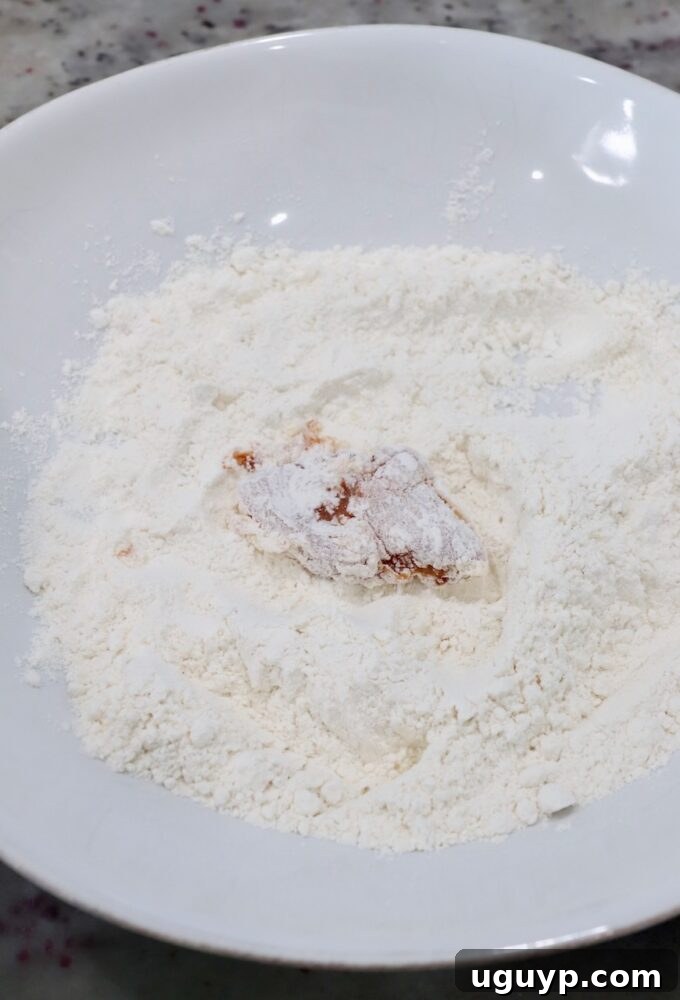 a piece of chicken breast fully covered in flour in a bowl