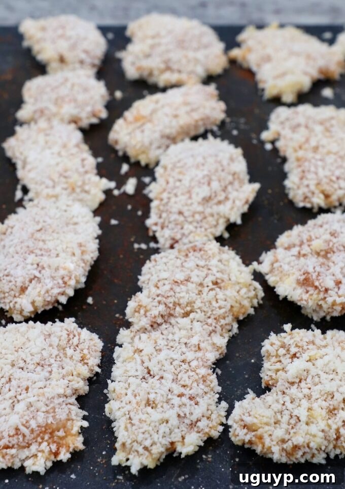 multiple pieces of breaded chicken laid out on a cutting board, ready for cooking