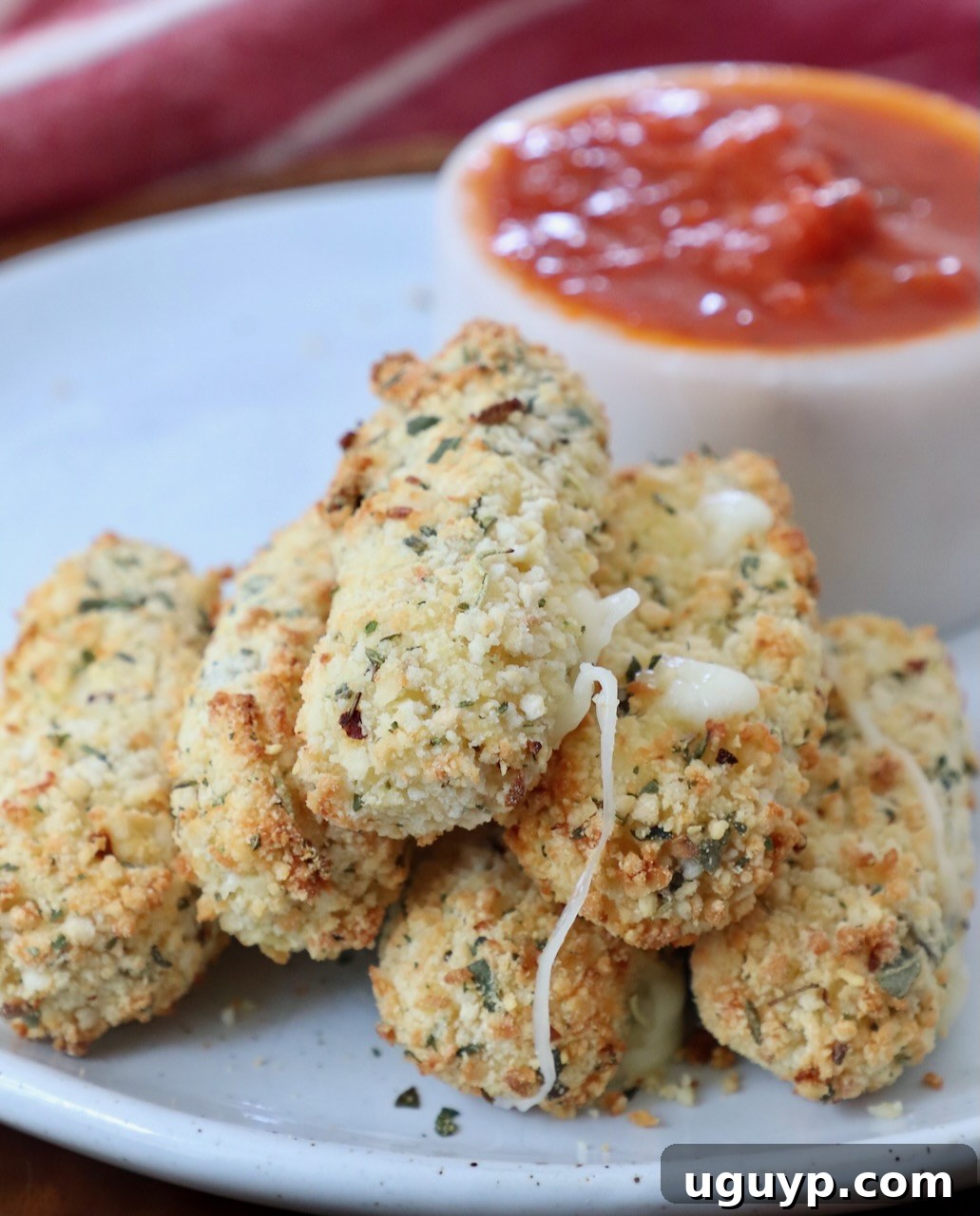 cooked mozzarella sticks stacked up on plate with small bowl of marinara sauce