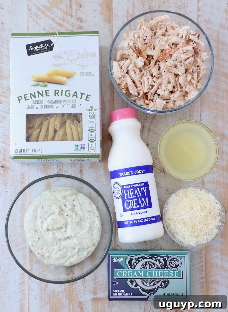 Various fresh ingredients for garlic parmesan chicken pasta, including cream cheese, parmesan, chicken, pasta, and sauce, laid out on a white wooden board.