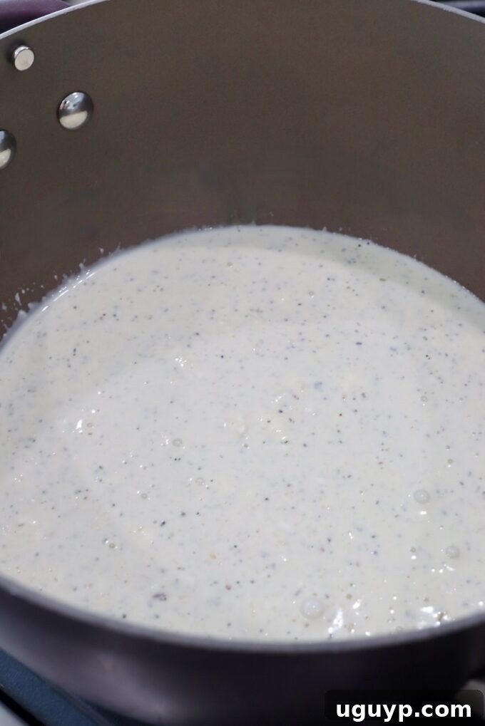 Garlic parmesan white sauce simmering in a saucepan, looking creamy and ready for chicken.