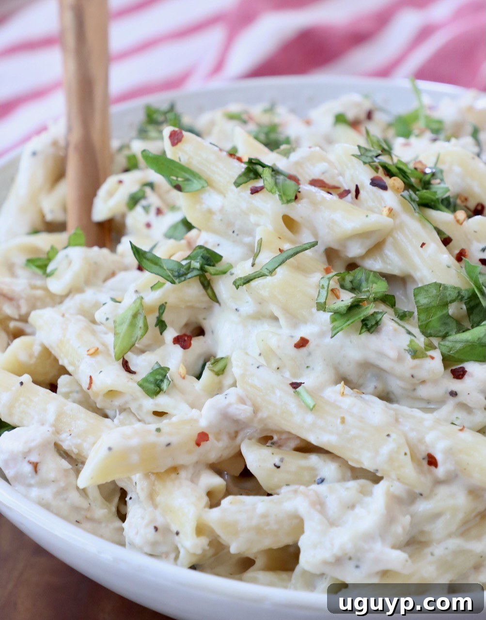 Close-up of creamy pasta tossed with chicken in a bowl, with a serving spoon, highlighting the rich sauce and perfectly cooked noodles.