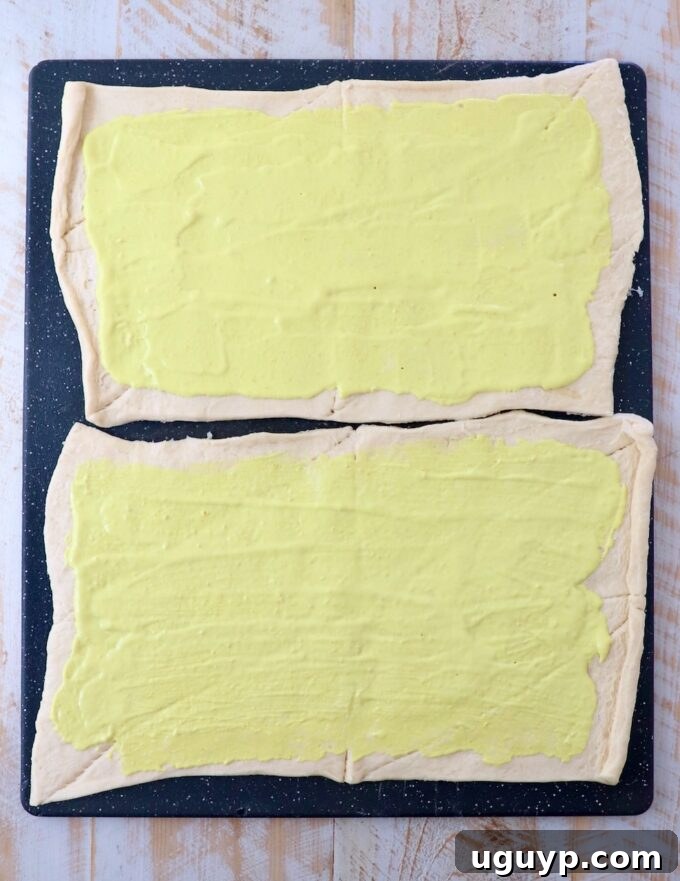 mayonnaise and mustard combined and spread on sheets of crescent roll dough on a large cutting board