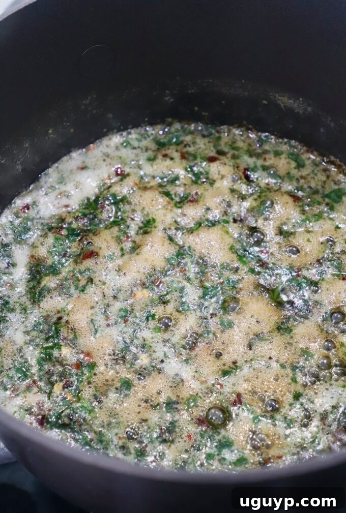 Melted butter infused with chopped herbs and spices simmering in a small saucepan.