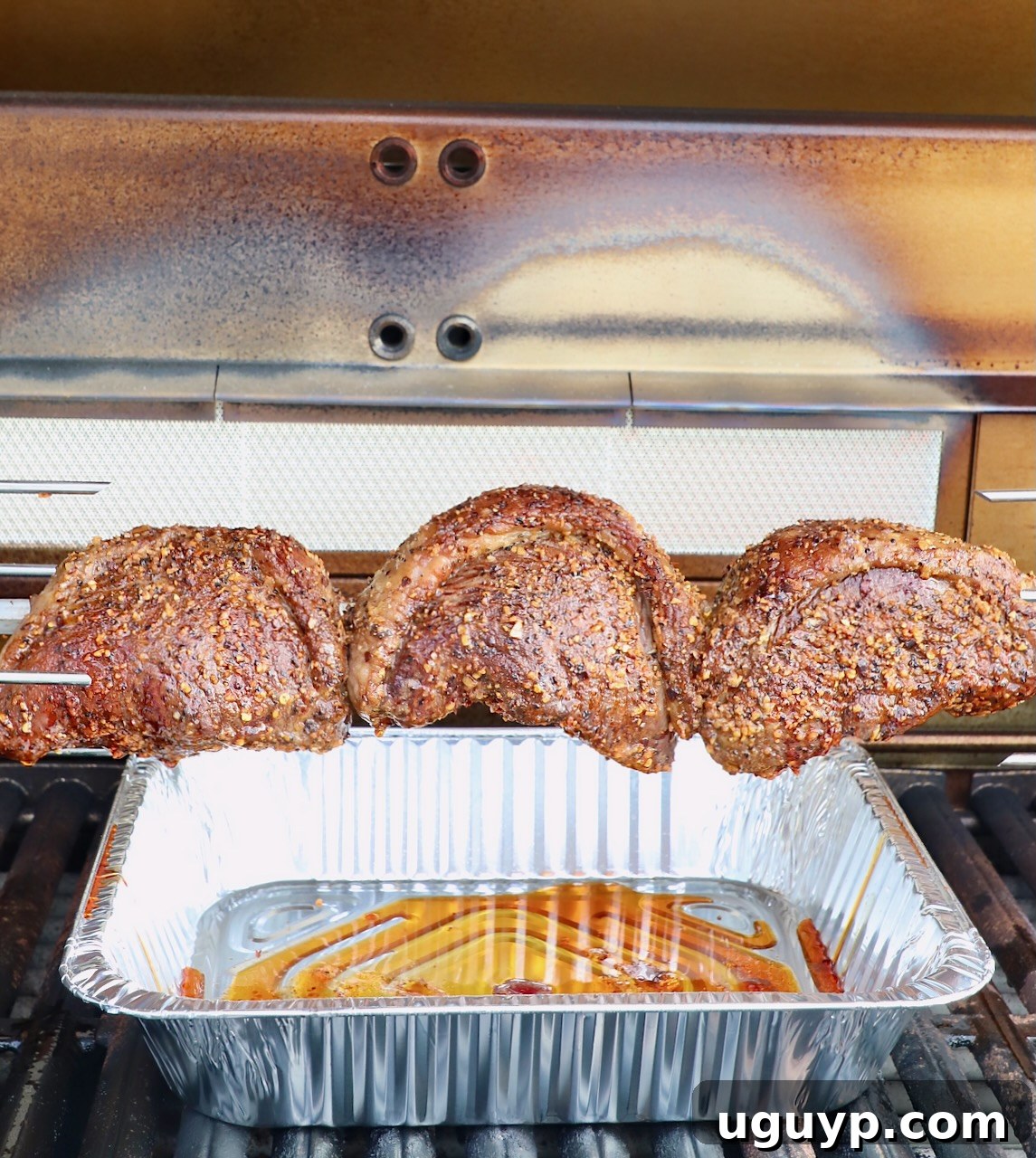 Three C-shaped picanha steaks rotating beautifully on a rotisserie rod in an outdoor grill, showcasing a perfect golden-brown sear.
