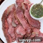 Thinly sliced cooked picanha steak on a plate with a small bowl of chimichurri sauce on the side.