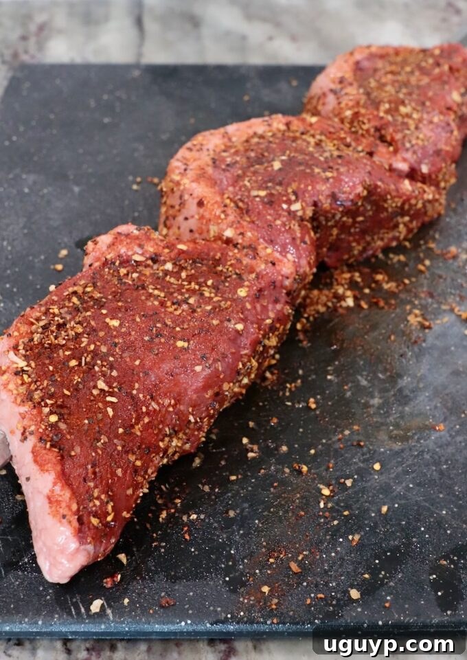 Uncooked picanha steaks generously seasoned with coarse salt and pepper on a cutting board.
