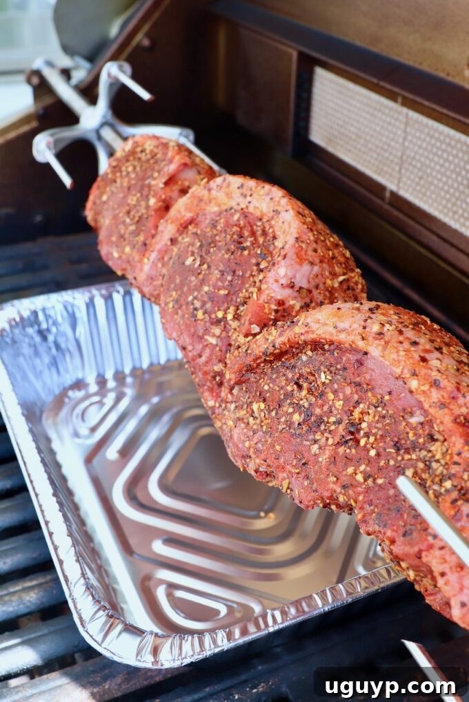 Uncooked, seasoned picanha steaks on a rotisserie rod, mounted in an outdoor grill, ready to cook.